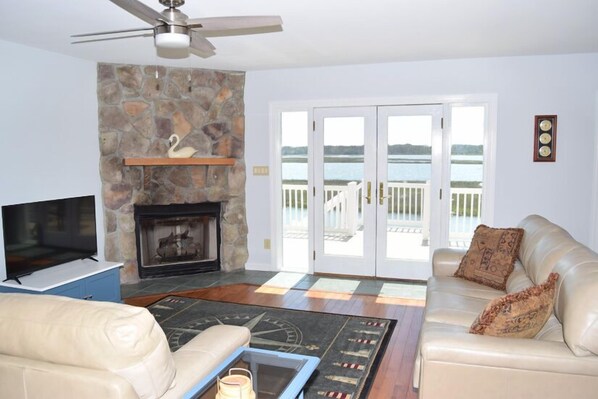 A living room with a stone fireplace, a television, a sofa, and a view of a lake through glass doors.