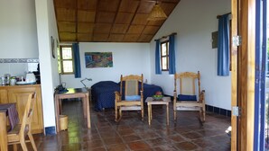 A room with a wooden ceiling, tiled floor, a bed with a blue bedspread, two wooden chairs, a small table with a lamp, and a window with blue curtains. - VillasvistaMasaya, double detached bungalow with access to swimming pool (Masatepe)