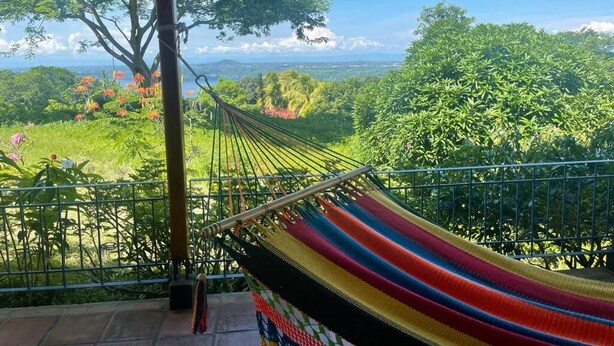 A hammock on a balcony overlooking a lush landscape with trees and a view of distant hills. - VillasvistaMasaya, double detached bungalow with access to swimming pool (Masatepe)