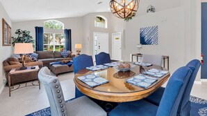 Ein modernes Wohnzimmer mit einem runden Glastisch, blauen Polsterstühlen, einem braunen Sofa und einer dekorativen Globenlampe.