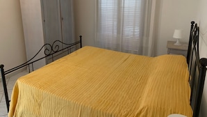 Un dormitorio con cama, armario, mesita de noche y ventana con cortinas.