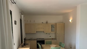 Una cocina compacta con servicios básicos, un comedor con mesa y sillas, y piso de baldosas.