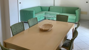 Un comedor con una mesa y sillas, un sofá verde y una cesta de mimbre sobre la mesa.