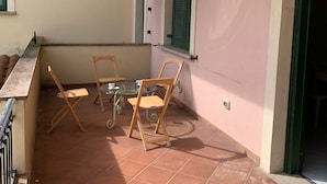 Un pequeño patio al aire libre con una mesa y cuatro sillas, una puerta y una ventana con contraventanas.