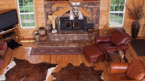 L’intérieur d’une cabane en rondins, avec une cheminée en pierre, des meubles en cuir et un grand tapis en peau de vache.