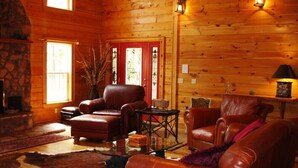 L’intérieur chaleureux d’un chalet en rondins, avec des meubles en cuir, une cheminée en pierre et un plafond en bois.