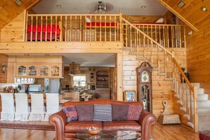 A spacious loft-style living area with a wooden staircase, a dining area, and a kitchen. - Large Cabin in the Kiamichi Wilderness (Rattan)