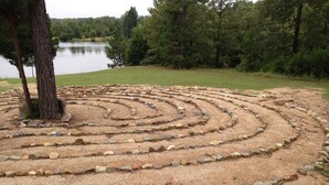 Un labyrinthe fait de pierres et de gravier, entouré d’arbres et bordé d’une étendue d’eau.