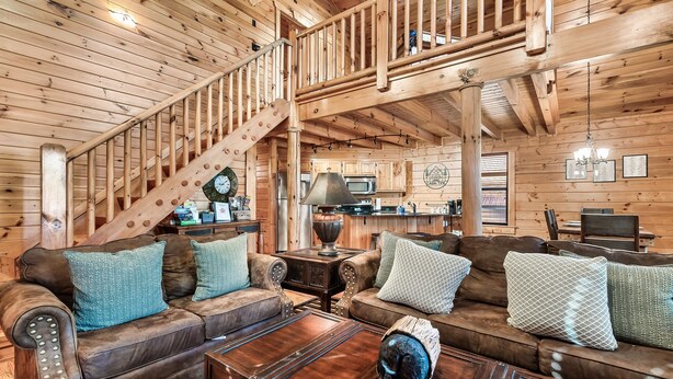 A wooden interior with a staircase, leather sofas, a wooden coffee table, and a kitchen area.
