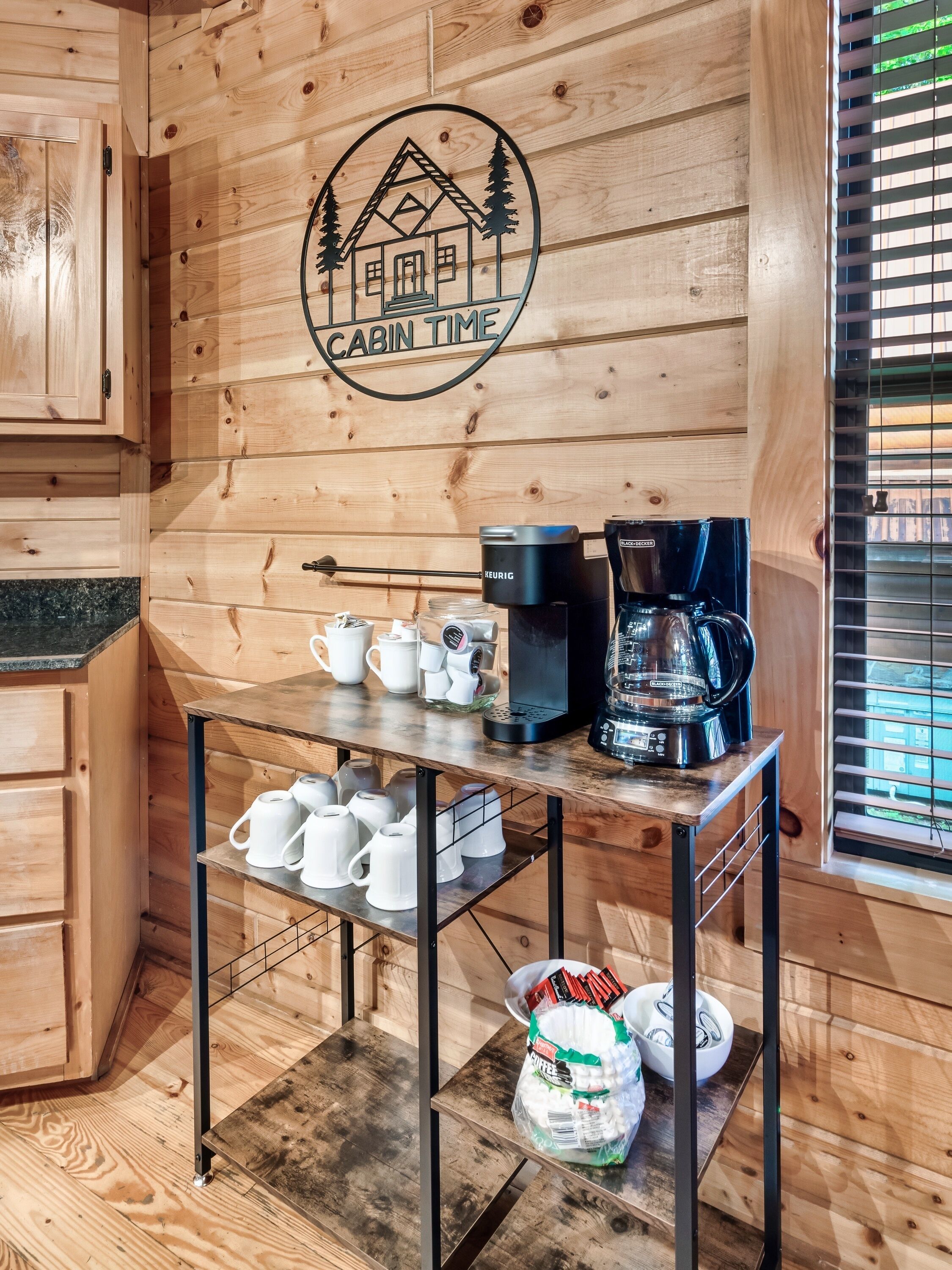 L’intérieur d’un chalet en bois, avec un coin café, une pancarte indiquant « TEMPS DE DÉTENTE AU CHALET » et une fenêtre avec des stores.