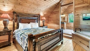 Une chambre dans une cabane en bois, avec un grand lit, deux lampes de chevet, un ventilateur de plafond et une vue sur l’extérieur.