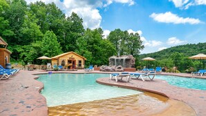 A swimming pool with lounge chairs, a wooden cabin, and a waterfall feature.