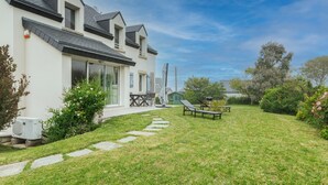 Une maison moderne avec une grande pelouse, une terrasse dotée de mobilier d’extérieur et un ciel dégagé.
