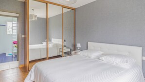 Une chambre moderne avec un grand lit, un dressing et une salle de bain visible à travers une porte ouverte.