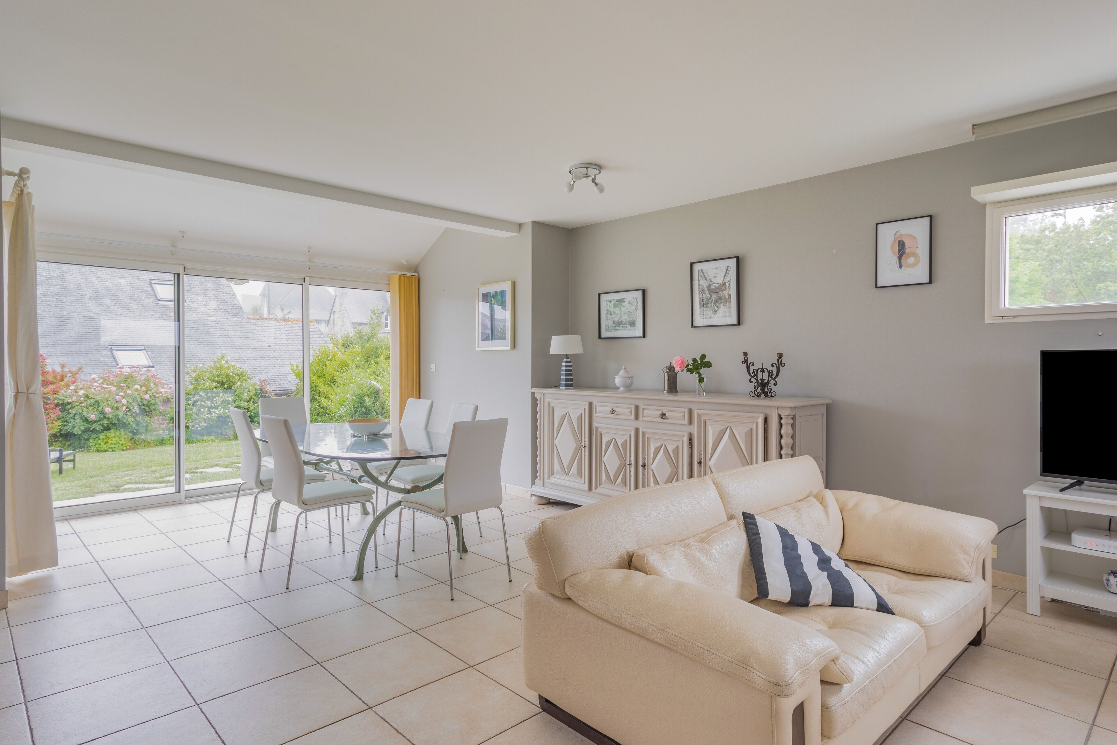 Un salon avec un canapé en cuir beige, un meuble pour la télévision, une table à manger avec des chaises et une porte vitrée donnant sur un patio.