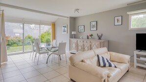 Un salon avec un canapé en cuir beige, un meuble pour la télévision, une table à manger avec des chaises et une porte vitrée donnant sur un patio.