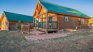 A log cabin with a green metal roof, a porch with a railing, and a small outdoor seating area. - Elk Hotspot w/ Views, Deck & Game Room (Estes Park)