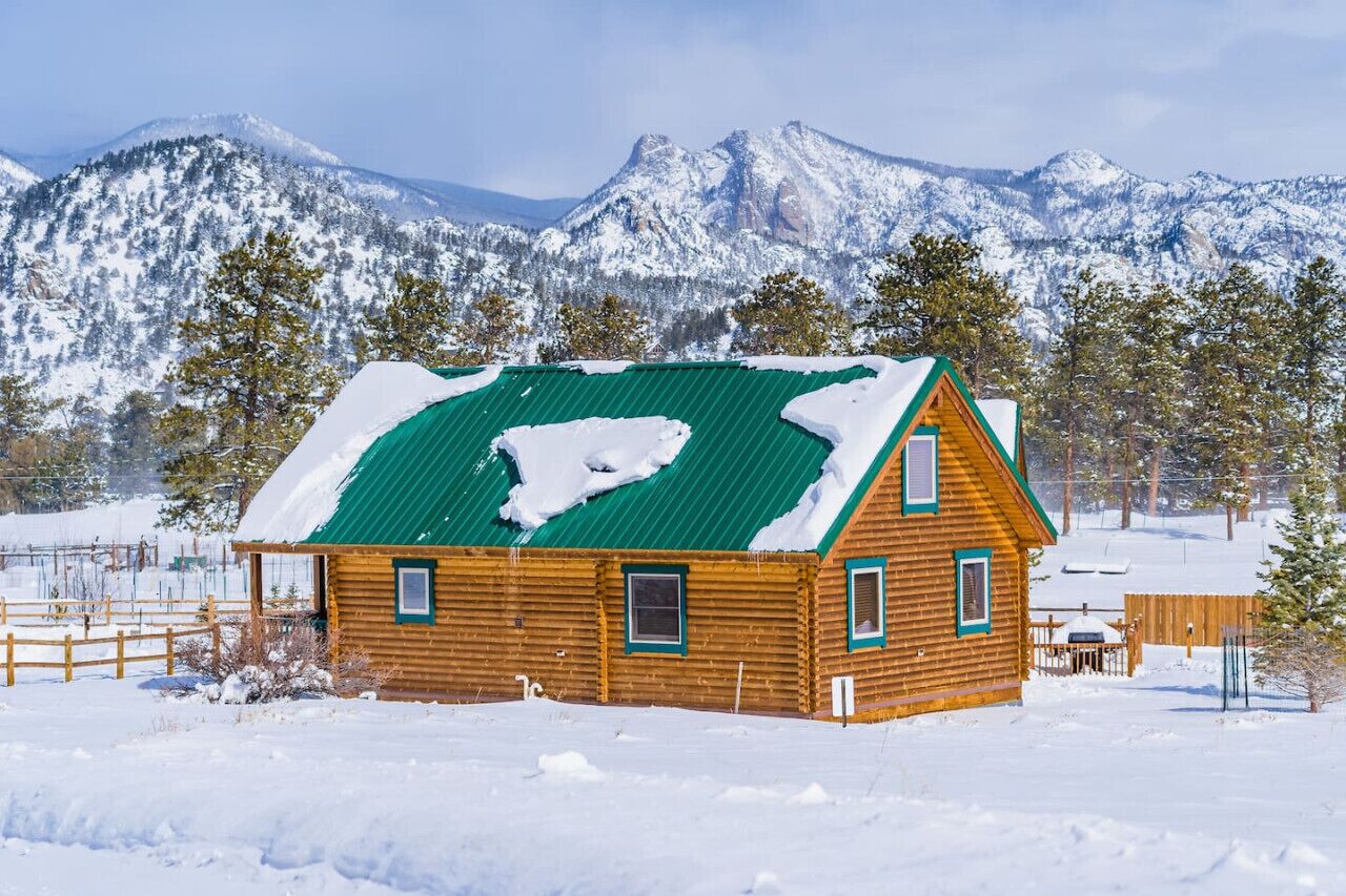A wooden cabin with a green roof, surrounded by snow-covered mountains and trees.