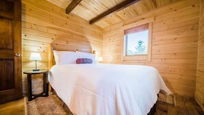 A wooden cabin bedroom with a bed, a nightstand, a window, and a door. - Elk Hotspot w/ Views, Deck & Game Room (Estes Park)