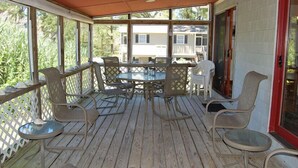 Eine überdachte Terrasse im Freien mit Tisch und Stühlen, einer Holzterrasse und Blick auf ein Haus im Hintergrund.