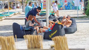 Een strandscène met mensen die ontspannen op luchtbedden, sommigen met parasols.