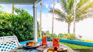 Une table avec vue sur un paysage tropical, deux boissons orange, une assiette de fruits et un magazine.