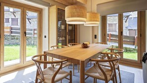 A modern dining area with a wooden table and chairs, large windows, and a hanging light fixture. - Luderna - Apartamento con jardín Crabera (Arties)