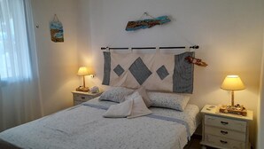 A neatly made bed with a white and blue patterned bedspread, two bedside tables with lamps, and a wall hanging above the bed. - L'oasi DI Orosei (OROSEI-NUORO)