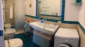 A bathroom with a toilet, bidet, sink, and washing machine. - L'oasi DI Orosei (OROSEI-NUORO)
