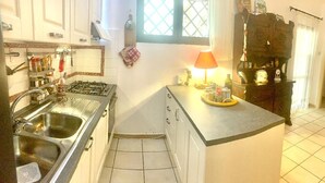 A compact kitchen with a gas stove, double sink, and a small countertop with a lamp. - L'oasi DI Orosei (OROSEI-NUORO)