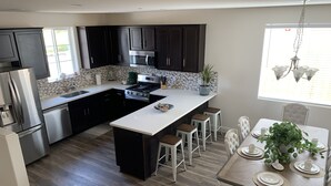 Een moderne keuken met donkere kasten, roestvrijstalen apparatuur, een centraal eiland met krukken en een eethoek met een tafel voor vier personen.