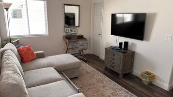 A living room with a grey sectional sofa, a TV, a wooden desk, and a large mirror.
