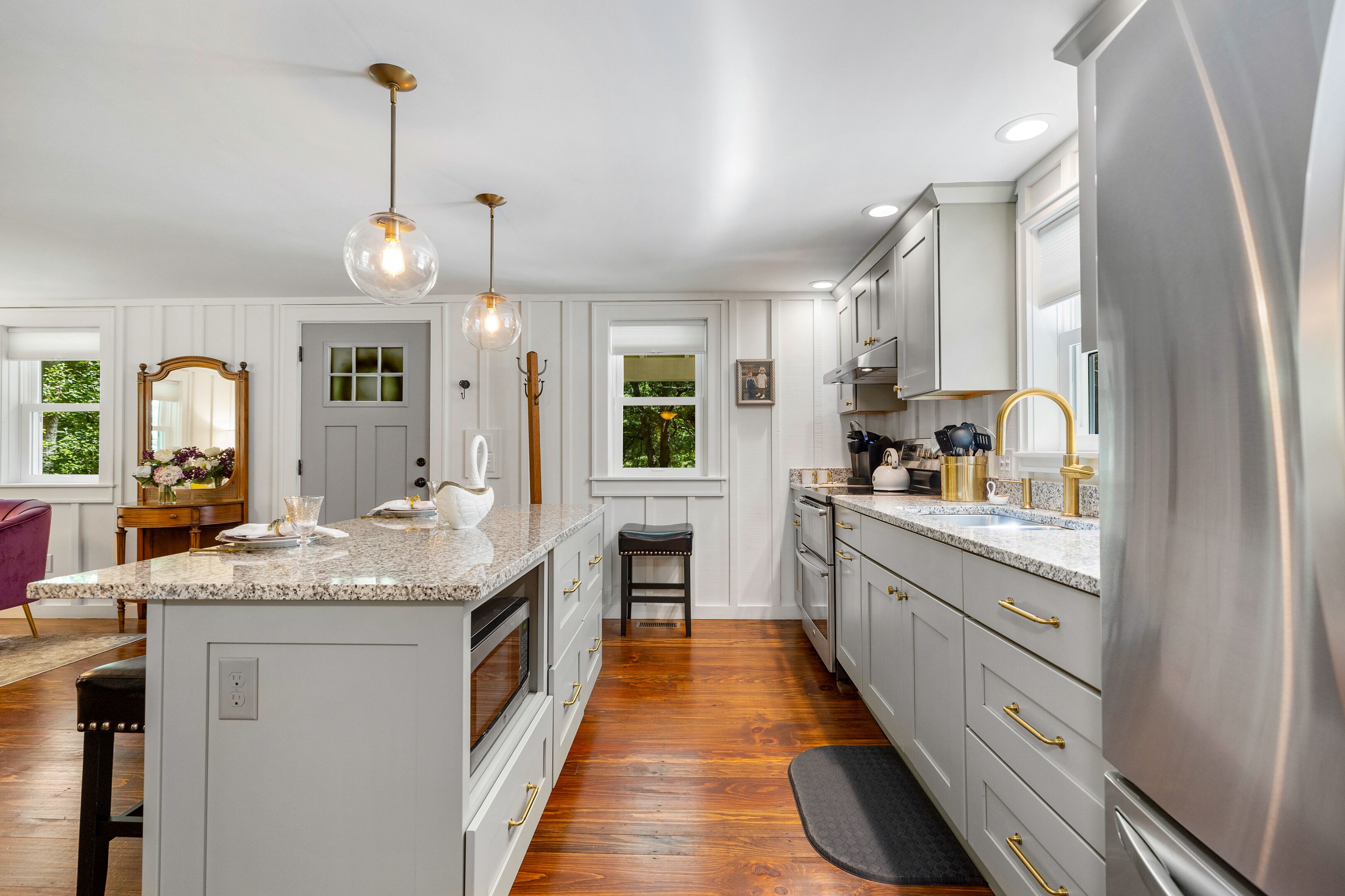 A modern kitchen with a central island, stainless steel appliances, pendant lighting, and a view to the outdoors.