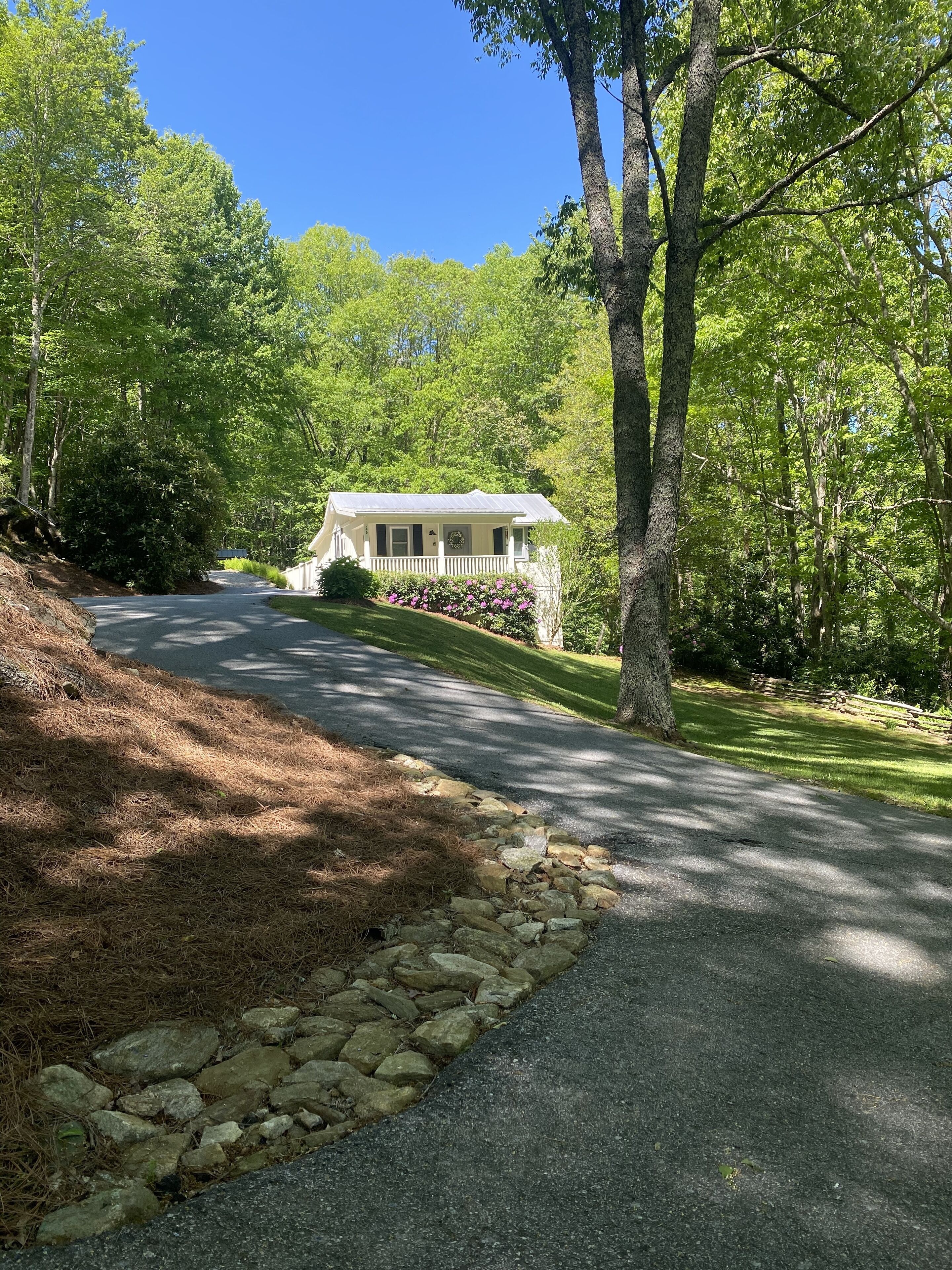A house with a stone pathway leading to it, surrounded by trees and a well-maintained lawn.