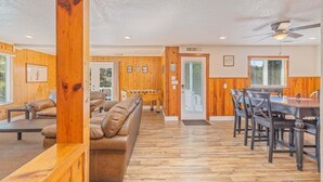A spacious living room with a wooden floor, a sofa, a dining table with chairs, and a foosball table.