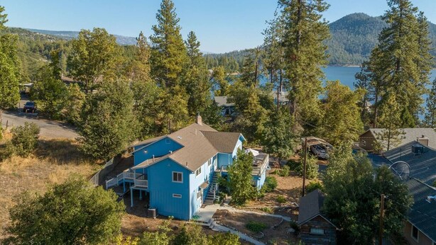 A blue house with a deck, surrounded by trees and a lake.