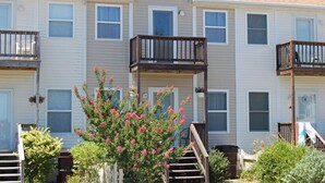 Un immeuble résidentiel à plusieurs étages, doté de balcons, d’une entrée principale et d’un petit jardin agrémenté de plantes à fleurs.