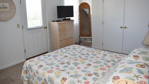 Une chambre à coucher comprenant un lit, une commode, un téléviseur, un miroir et une armoire.