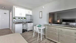 Une cuisine moderne avec des meubles blancs, une table à manger avec des chaises et un grand téléviseur fixé au mur.