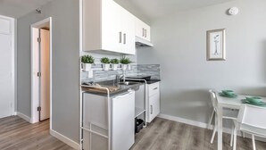 Une cuisine moderne avec des meubles blancs, une cuisinière encastrée et un coin repas comprenant une table et des chaises blanches.