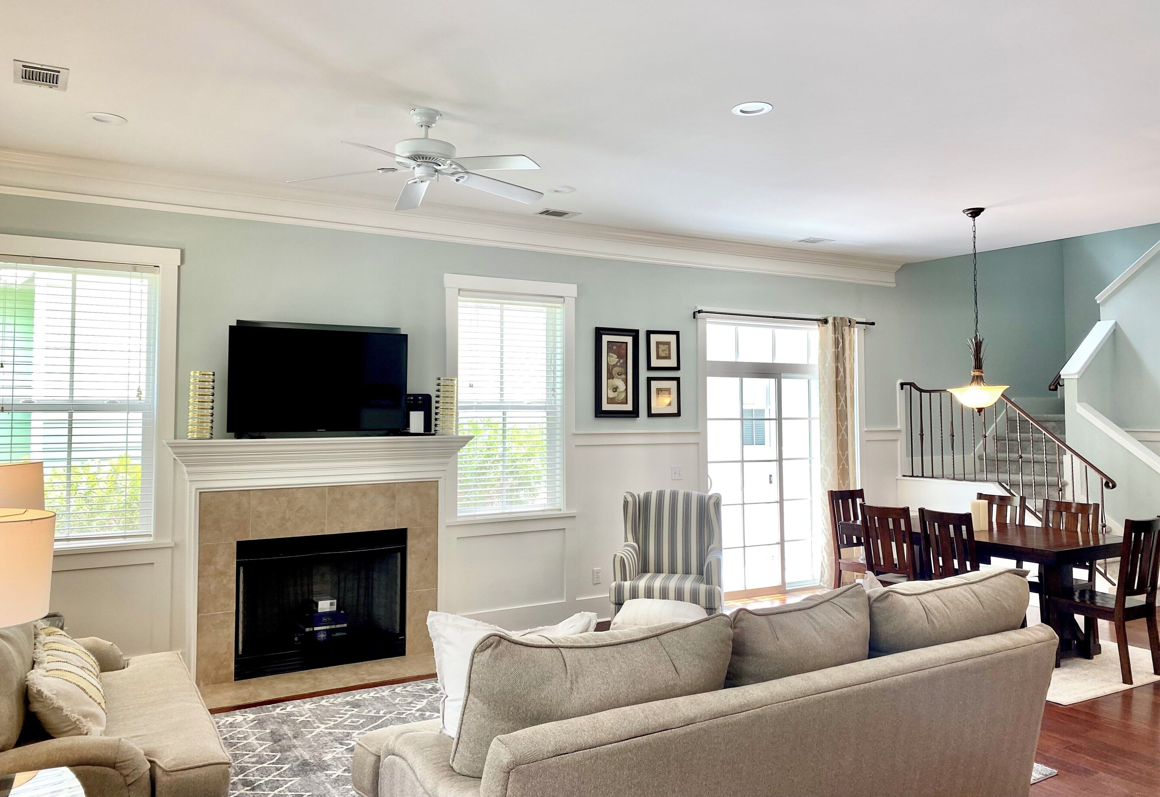 A living room with a fireplace, a television, a sofa, a striped armchair, and a dining area with a staircase.