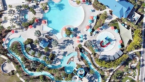 An aerial view of a resort with a large central pool, multiple smaller pools, and a winding water slide. - No Rear Neighbors • Private Pool • Foosball • Lazy River • Near Disney (Davenport)