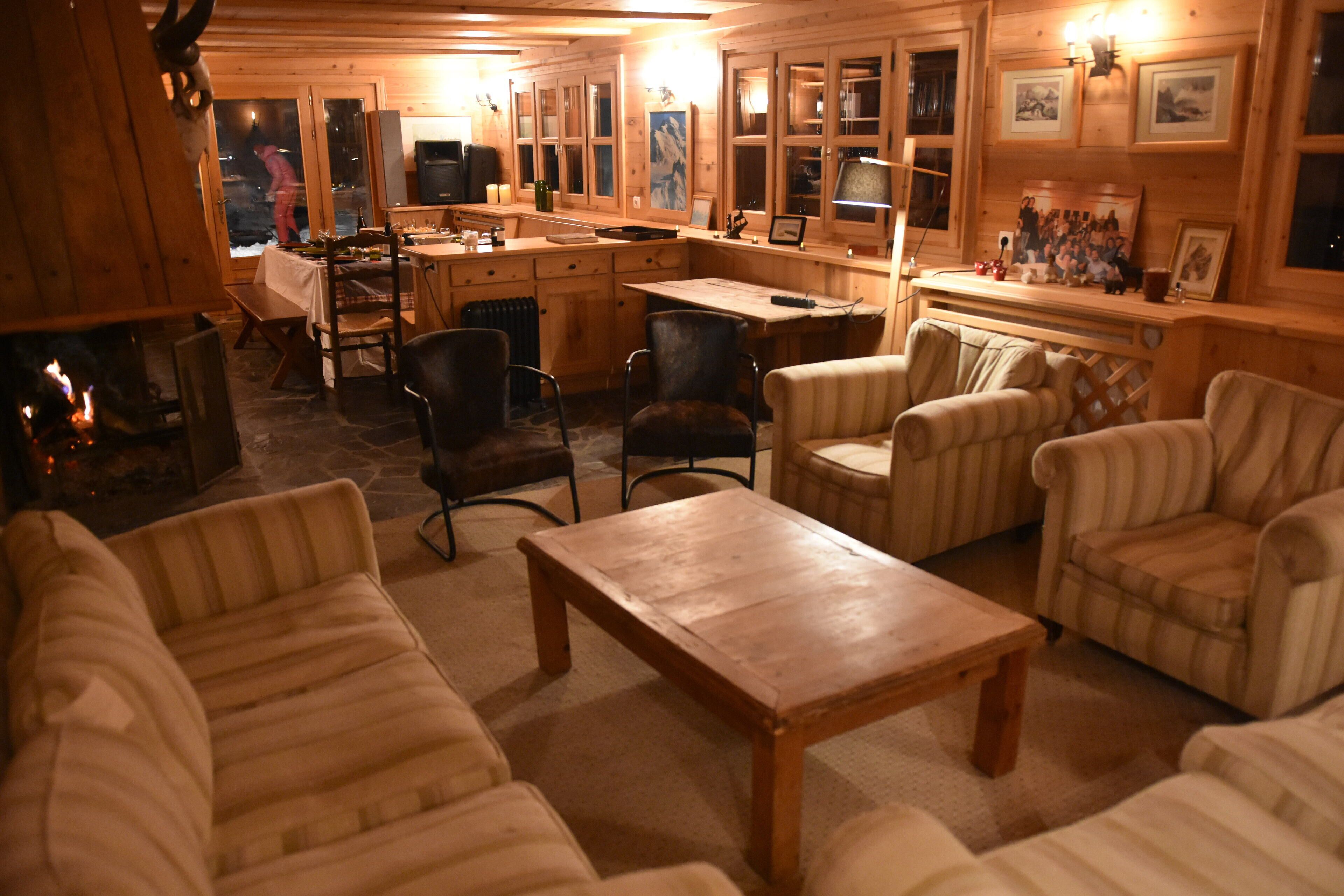A cozy wooden cabin interior with a fireplace, comfortable seating, a dining area, and a kitchen.