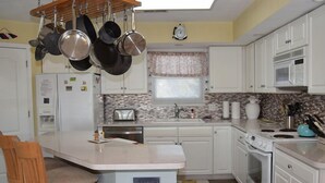 Una cocina con armarios blancos, una isla central, ollas colgantes, un microondas y una estufa.