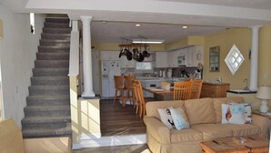 Un amplio salón con una escalera, un sofá color beige, una mesa de centro de madera y una cocina al fondo.
