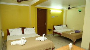A hotel room with two beds, each with a brown bedspread and white pillows. There are two white swan-shaped towels on the beds. A wooden table with a glass and a napkin is in the room. - Hotel Nandha (Karaikal)