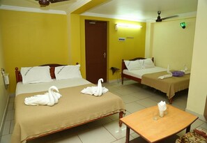 Habitación de hotel con dos camas, cada una con cubrecama marrón y almohadas blancas. Hay dos toallas en forma de cisne blanco sobre las camas. En la habitación hay una mesa de madera con un vaso y una servilleta.
