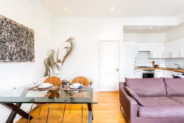 Un espacio de estar moderno con una mesa de comedor de vidrio, un sofá y una cocina al fondo.