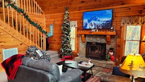 Ein gemütliches Blockhaus-Interieur mit Kamin, Weihnachtsbaum, Fernseher und einer Treppe.