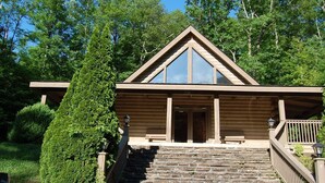 Eine Holzhütte mit einer Steintreppe, die zu einer Haustür führt, umgeben von üppigem Grün.